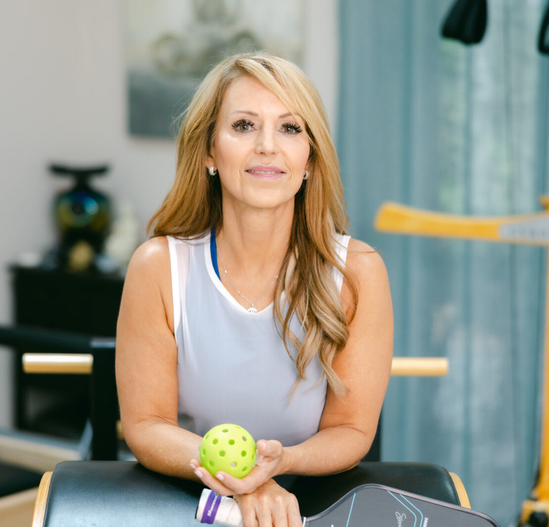 Headshot of Shannon Willits, a smiling Pilates instructor wearing a professional fitness outfit, against a neutral background, embodying confidence and approachability.